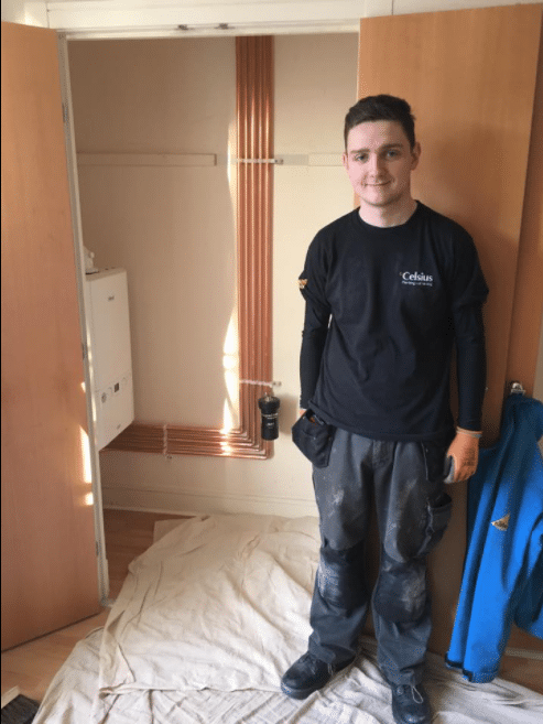 Apprentice Plumbing & Heating Engineer standing next to a new boiler replacement.