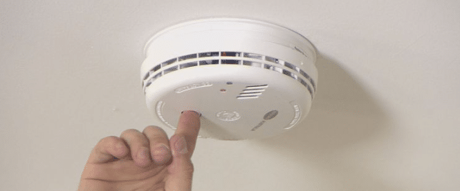 Person pushing the test button on a smoke detector